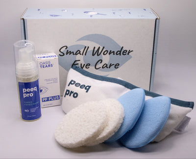 Small Wonder Eye Care eye makeup remover kit including a blue and white spray bottle, a box of Class Tears, a white applicator pouch, and three cleansing pads (one white, two light blue) on a light gray background.